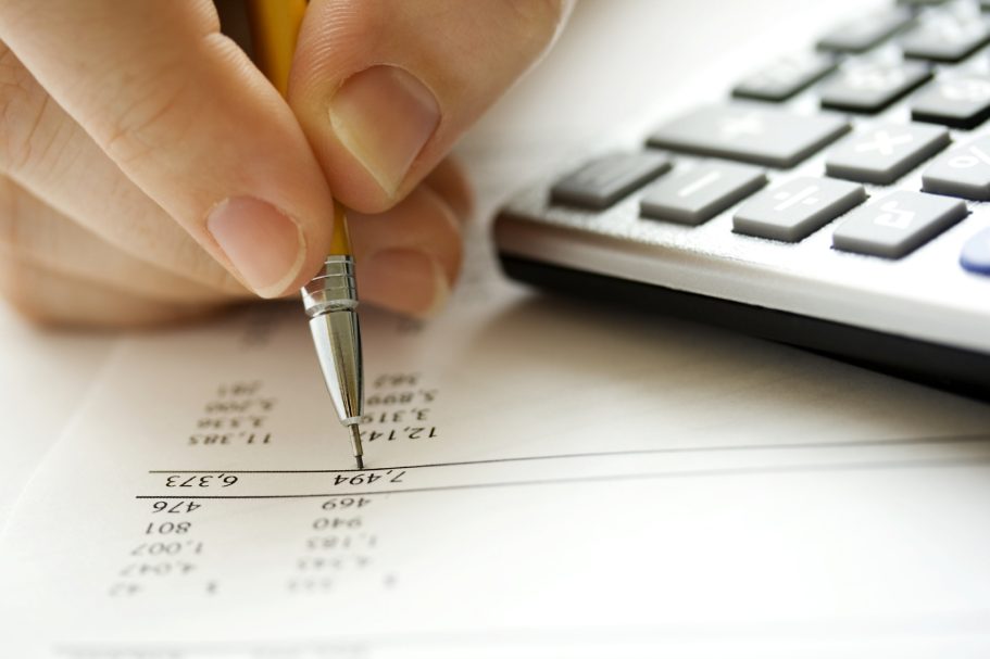 comptabilité Une main tenant un stylo, écrivant sur un document à côté d'une calculatrice.