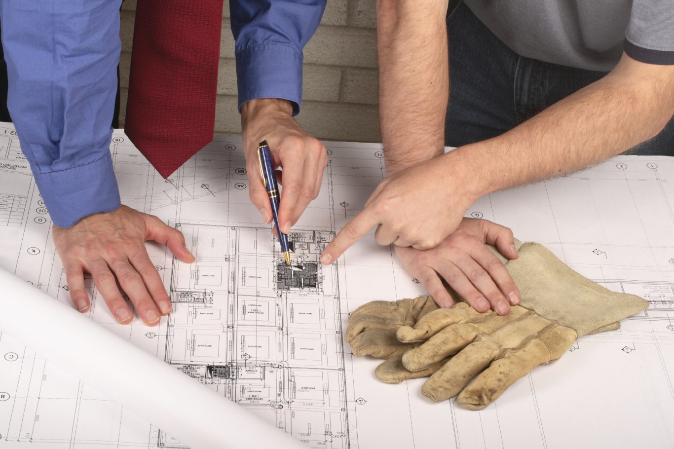 Informatique Deux personnes examinant des plans de construction, gants de travail à proximité.