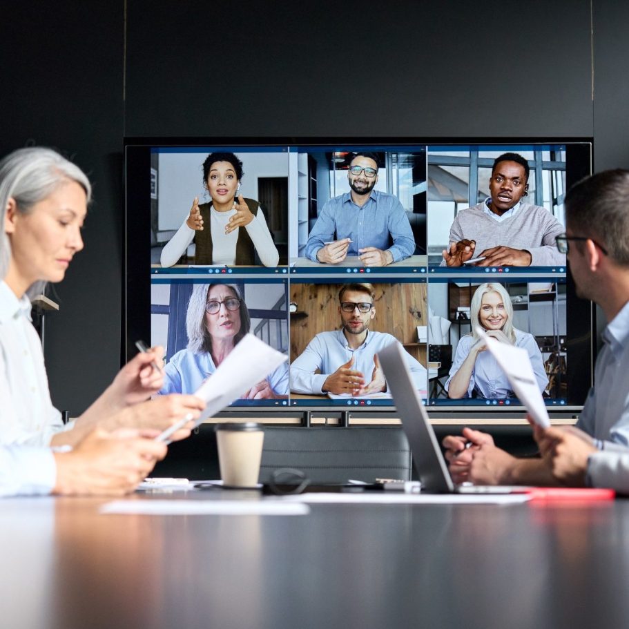 cession et transmission Réunion hybride avec des participants virtuels sur un écran et des personnes en présentiel.