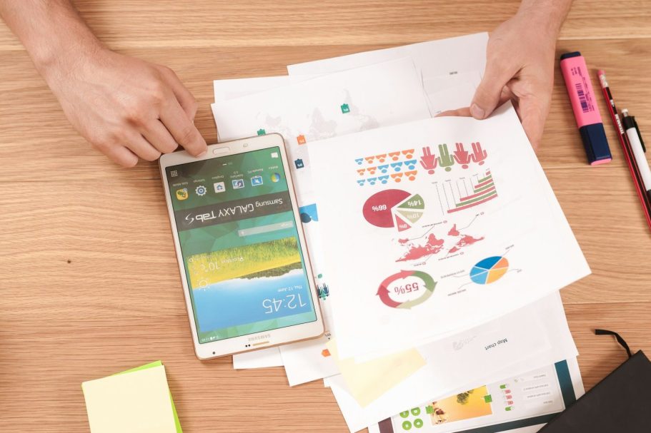 audit Main d'une personne tenant une tablette, entourée de graphiques et de documents sur une table.