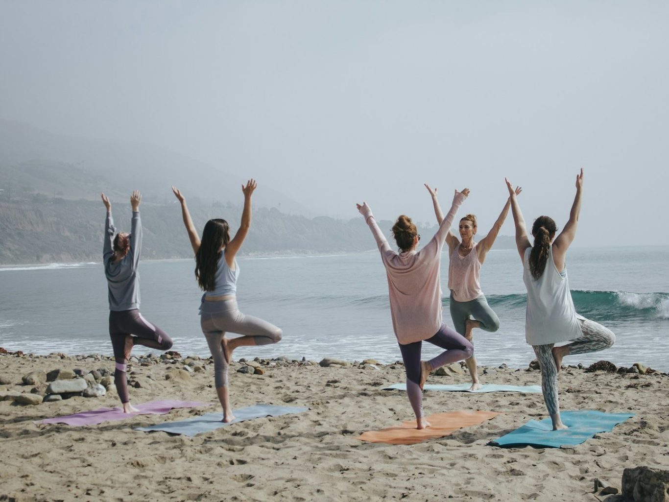 ateliers Groupe de personnes pratiquant le yoga sur la plage, avec la mer en arrière-plan.