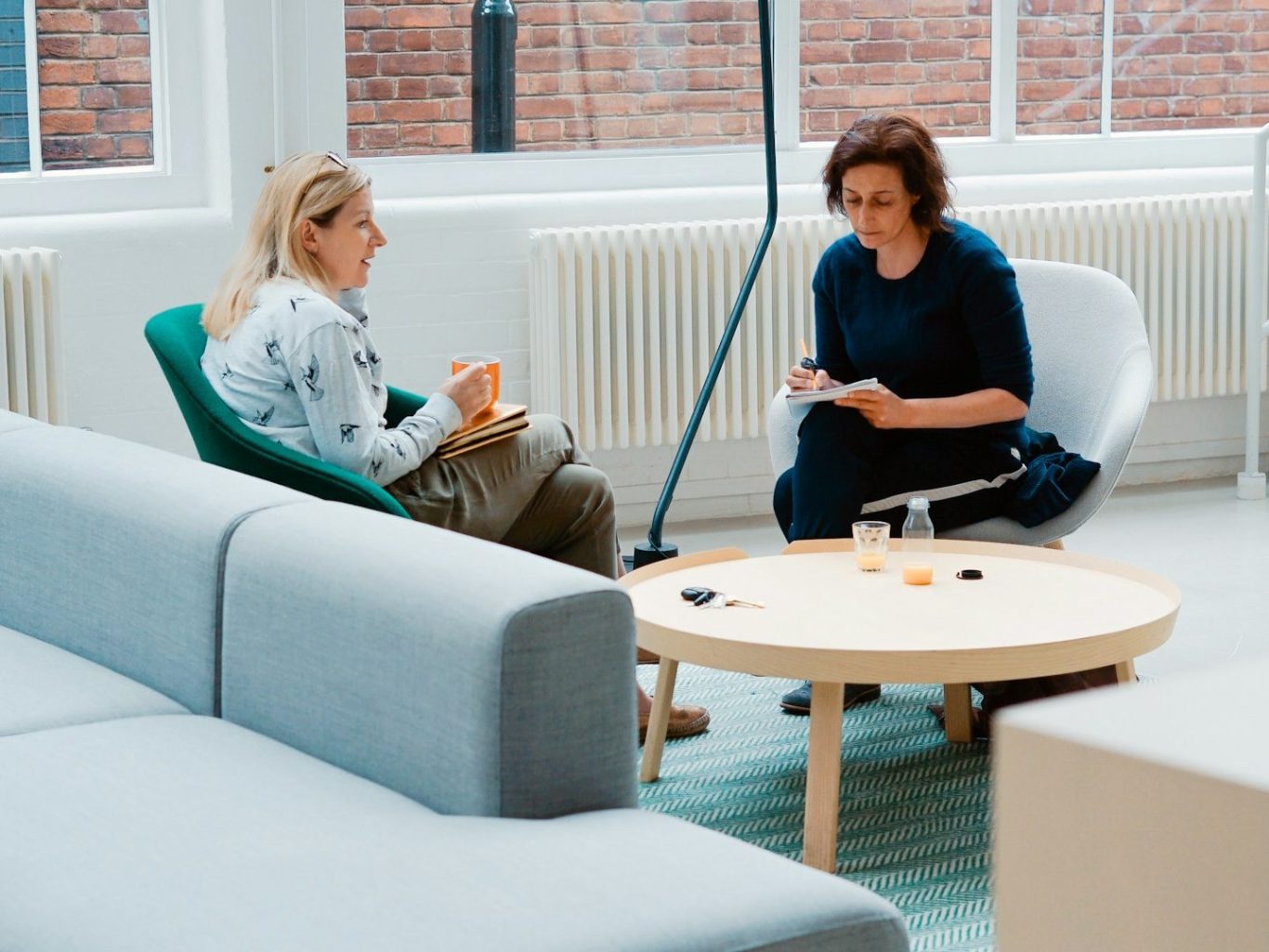 coach Deux femmes discutent assises sur des fauteuils autour d'une table basse dans un intérieur lumineux.